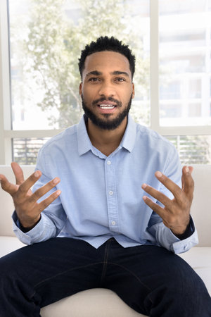 Vertical webcam view man take part in virtual meeting using application, sit on sofa at home lead remote conversation by business, record video vlog, participate in webinar share skill and experienceの写真素材