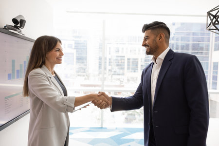Two happy confident diverse business partners shaking hands at presentation board with marketing analytic chart, getting agreement, starting collaboration, partnershipの写真素材