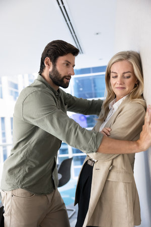 Young male boss harassing embarrassed female coworker, young employee in office, imposing flirt, hug, dating, using inappropriate behavior, practicing sexual harassment at work. Vertical shotの写真素材