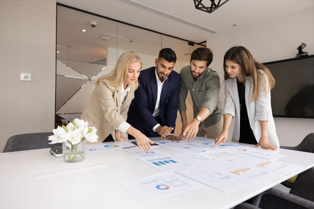 Diverse team of marketing professionals working on paper analytic reports together, pointing at charts on meeting table, analyzing startup infographics, planning financial developmentの写真素材