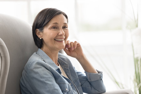 Golden years joy. Close up portrait smiling carefree aged lady retiree relax in soft armchair enjoy freedom domestic comfort spend happy days in retirement feeling healthy satisfied full of wellbeingの写真素材