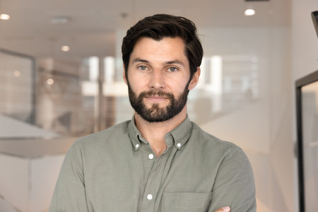 Serious confident 30s Caucasian business leader man posing for male head shot in office, looking at...