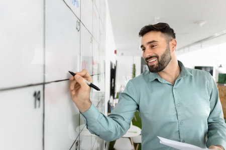 Task management. Happy smiling young business professional project leader entrepreneur organize workflow visual structure on monthly schedule marker board track milestones holding planning paper notesの写真素材