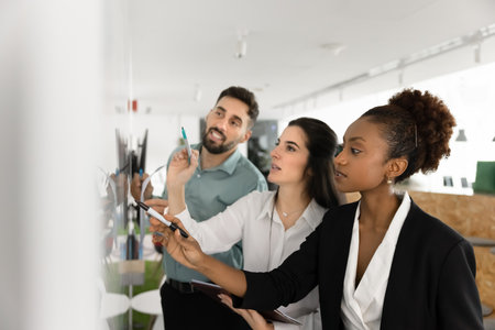 Creative professionals at collaborative work. Expert team three young diverse businesspeople manage tasks on workflow panel brainstorming strategy write ideas visualizations with markers. Copy spaceの写真素材