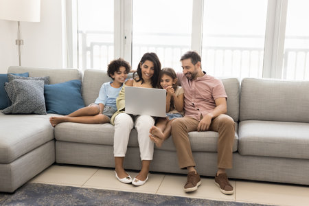 Modern family of four spending time together with laptop, watching movies or cartoons, exploring...