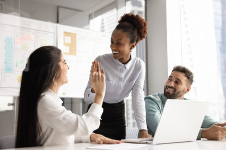 Leader encouraging progress. Happy cheerful young businesswoman mentor team lead giving high five to female teammate celebrate successful work achievement support great idea during project discussionの写真素材