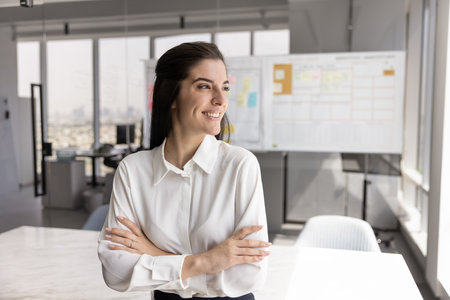 Inspired leadership. Confident smiling young woman business owner department director project executive stand at office workplace look at distance dream of financial growth create successful strategyの写真素材