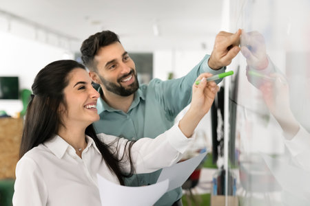 Planning with enthusiasm. Happy smiling 2 diverse marketing team members corporate planners review project timeline on glass marker board discuss key milestone on visual calendar enjoy completing taskの写真素材