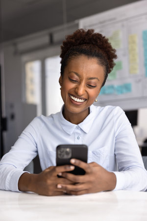 Digital break. Relaxed smiling young businesswoman office employee use app on mobile phone to contact friend check new messages in social media account write funny text to colleague in corporate chatの写真素材