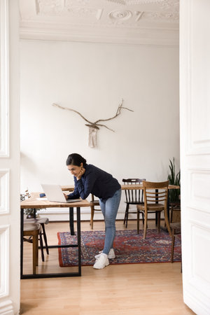 Digital project planning. Vertical shot busy focused young woman lean over work desk in cozy shared office space manage social media organize electronic files review startup presentation on notebookの写真素材