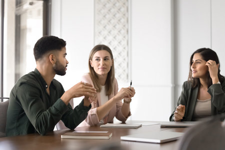 Three professionals engaged in brainstorming session, focused conversation seated at table, listening team leader explaining details, exchange opinion, presenting ideas or planning project togetherの写真素材