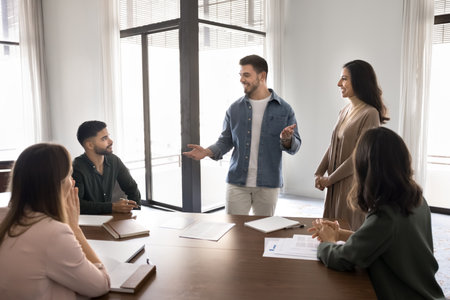 Young Arabian businessman speaking to group of seated colleagues in modern office conference room, introducing new employee, making presentation to team members. Seminar, educational event for staffの写真素材