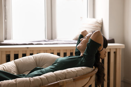 Fresh air wellness. Happy smiling young lady leaning back in rattan armchair facing light window relax satisfied with comfortable indoor climate enjoy breathing cool air wellbeing peace in cozy homeの写真素材