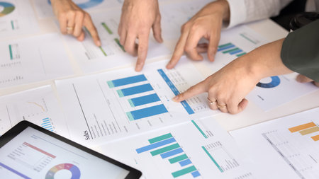 Cropped shot of paper sales reports and hands of four analysts pointing at statistic graphs....