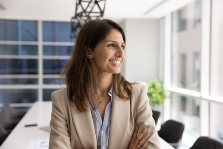 Cheerful young female executive woman posing in office conference room alone, standing with arms...
