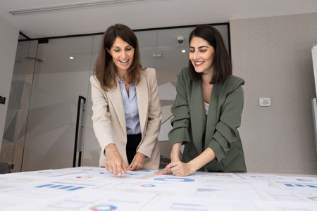 Happy successful female project managers reviewing paper marketing reports together, discussing creative ideas for product development, business strategy for growth, pointing at charts, talkingの写真素材