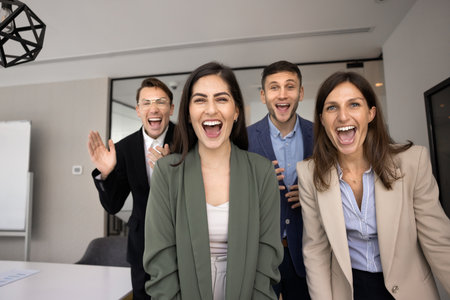 Four cheerful excited business colleagues laughing and shouting at camera, celebrating successful teamwork, company goal achievement, having fun, enjoying leisure togetherの写真素材