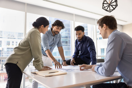 Creating project. Creative young multiethnic business team ahead with mid aged male leader engaged in paperwork at workplace desk discuss strategy plans brainstorm on startup idea analyze documentsの写真素材