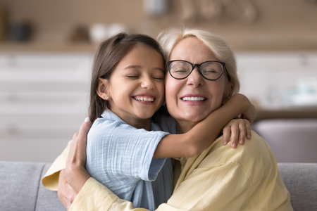Tender hugs. Close up portrait adorable kid granddaughter loving elderly grandmother cuddle with closed eyes on cozy sofa touch cheeks in pure serenity share affectionate sweet moment of bonding loveの写真素材