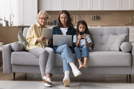 Digital addiction. Busy preteen girl millennial mom mature grandma rest together on sofa focused on...