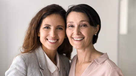Beauty and bond between generations. Head shot family portrait happy beautiful mature mom grownup daughter posing close together cuddling touching heads looking at camera with cheerful white smilesの写真素材