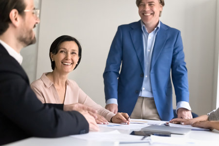 Friendly business collaboration. Joyful smiling mature male team leader engaged in casual conversation on office meeting with diverse colleagues laugh discussing project plan at staff briefing seminarの写真素材