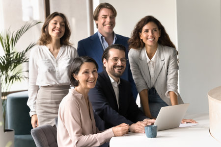 Confident department staff. Multiethnic team of business professionals with mid aged male leader boss pose at office desk with successful smiles united by shared goals strong motivation company valuesの写真素材