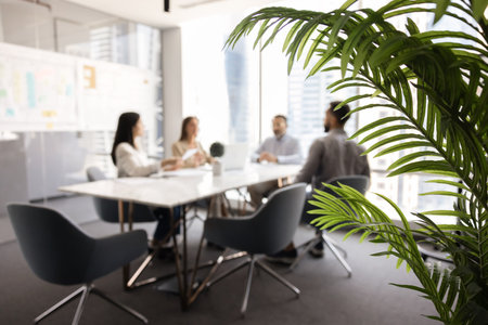 Blurred shot of four business colleagues talking at office meeting table, sitting at desk together,...