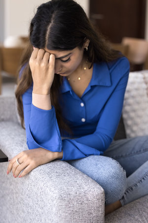 Depressed unhappy young Indian woman touching forehead, leaning head on hand, feeling bad, stressed, frustrated, suffering from anxiety, depression, migraine. Vertical shotの写真素材