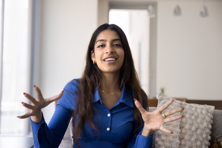 Happy excited Indian blogger woman looking at camera and speaking, moving hands, expressing emotions with gestures, smiling. Influencer broadcasting on Internet, posing for head shotの写真素材