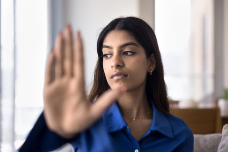 Serious concerned young Indian woman making stop hand, gesture symbolizing warning, danger, rejection, restriction, showing blurred palm at camera, looking away. Close up of armの写真素材