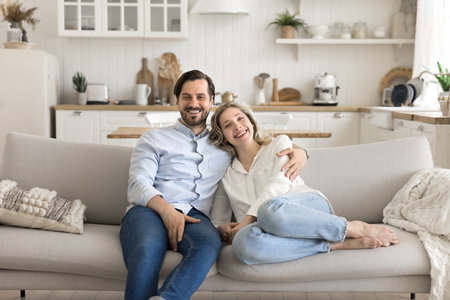 In love with life. Portrait happy smiling spouses mid aged husband wife rest on cozy sofa at modern kitchen hug look at camera enjoy calm peaceful weekend day togetherの写真素材
