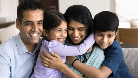 Close up of beautiful parents cuddling their loving little son and daughter seated on sofa at home, enjoying carefree leisure and quality time together, having good friendly, harmonic relationsの写真素材