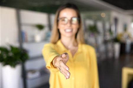 Positive young business professional woman giving hand for shaking at camera, offering job,...