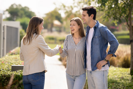 Real-estate agent greeting young couple standing outdoors in well-groomed landscaped area of residential complex with modern villas and houses, provide consultation, selling property, start meetingの写真素材