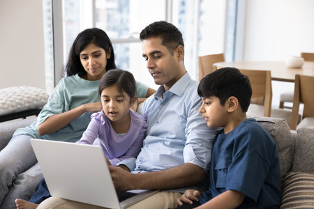 Indian couple with two little kids using laptop at home, choosing goods, making order, purchasing...