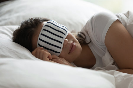 Comfortable and serene sleep. Side view portrait carefree millennial woman sleeping in cozy bed at domestic bedroom or hotel suite covering eyes with soft mask creating darkness for deep relaxing restの写真素材