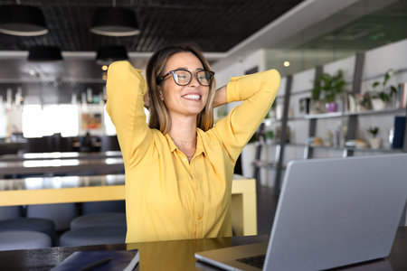 Cheerful satisfied young business professional woman getting relaxed in co-working, stretching body at workplace with laptop, keeping hand on nap with open elbows and closed eyesの写真素材
