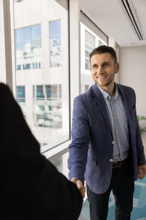 Businessman shaking hands colleague stands un modern workspace. Sales manager, financial advisor or executive greeting client, starting or finalizing formal meeting in company office. Deal, etiquetteの写真素材