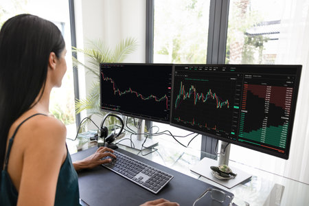 Two large monitors of young trader woman working from home, analyzing financial graphs, managing...
