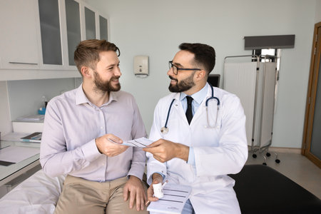 Pharmaceutical consultation. Smiling young man patient take paper drug receipt prescription note from trusted doctor listen to recommendations on correct medication use proper safe dosage therapy planの写真素材