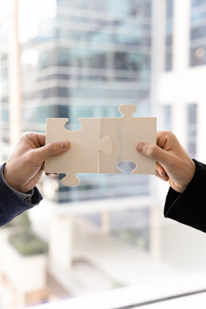 Two male hands connect white puzzle pieces, bring them together in perfect alignment, symbolizing...