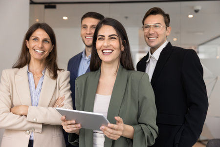 Happy Hispanic businesslady holds digital tablet posing with diverse teammates, colleagues in modern...