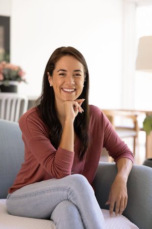 Happy middle-aged 40s millennial woman dressed in casual clothes sitting comfortable on cozy couch...