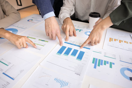 Close-up shot of hands of business colleagues pointing at various printed bar charts and graphs...