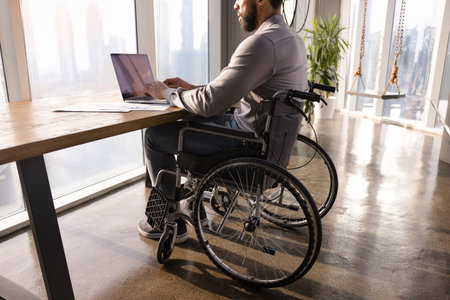 Cropped shot of African businessman with paraplegia working at computer in office with accessible...