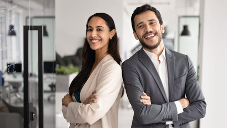 Two young 30s multiethnic teammates, creative department staff members posing in modern office, exuding competence and professionalism. Teamwork, team unity, togetherness and successful partnershipの写真素材