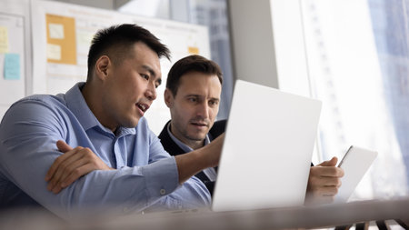 Multiracial focused teammates, partners solving business-related matters in office using digital...