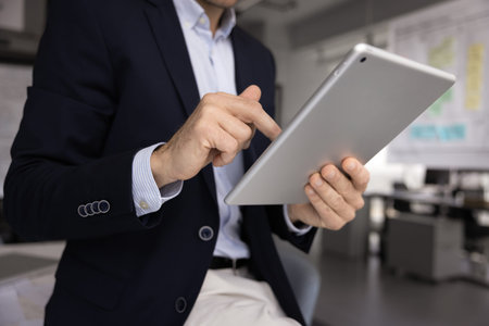 Close up cropped view of businessman using digital tablet in modern office, reviewing financial data or preparing online presentation for upcoming meeting, making data analysis or responding to clientの写真素材