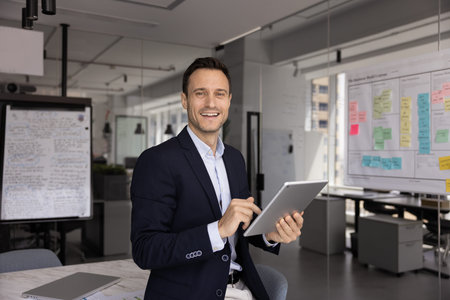 Office portrait of smiling middle-aged businessman, project manager or analyst in suit looking at camera, holding digital tablet, enjoy online workflow, using new AI, innovative business technologiesの写真素材